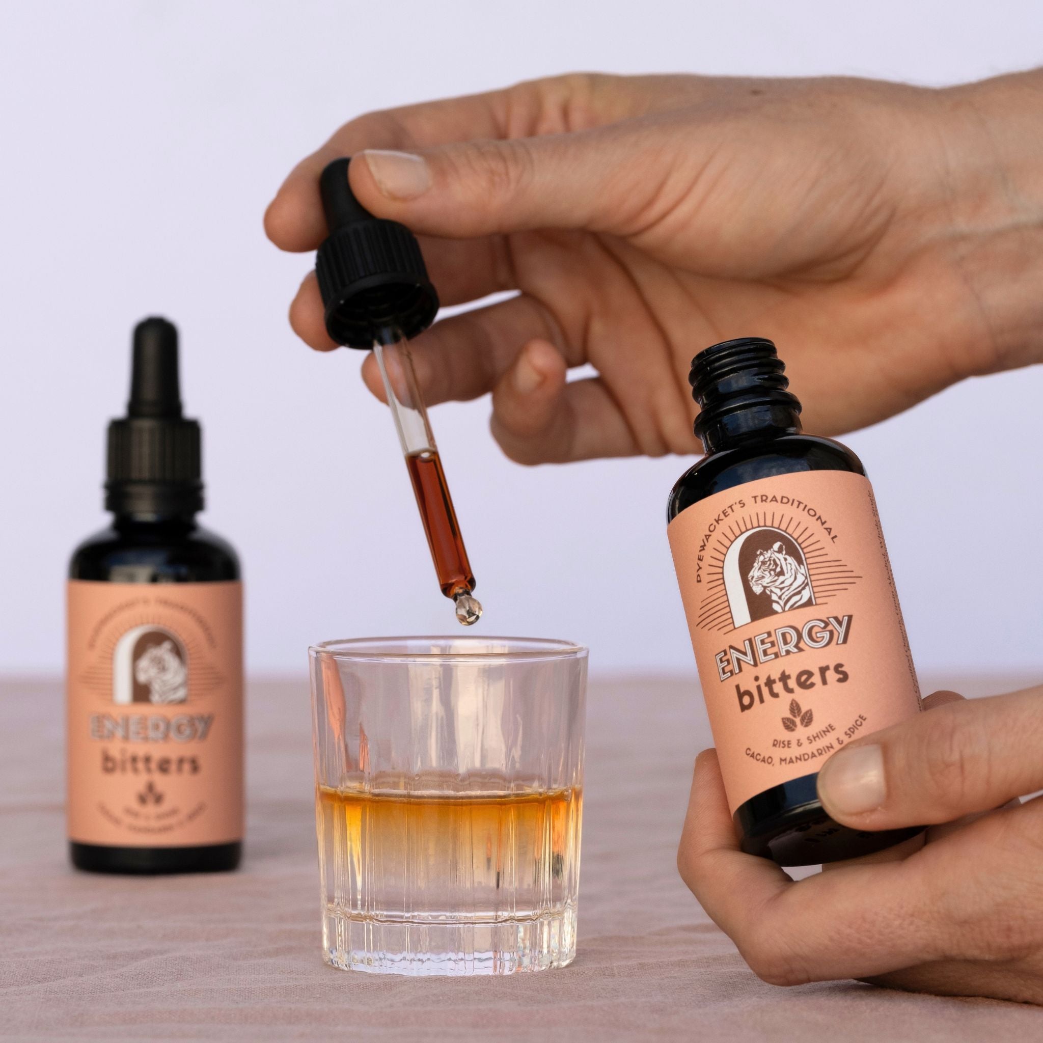 Person using a dropper to add bitters into a glass with two bottles of &