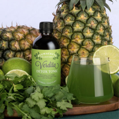 Bottle of Verdita Detox Tonic with a pineapple, lime, and glass of green verdita tonic and soda water on a wooden board.